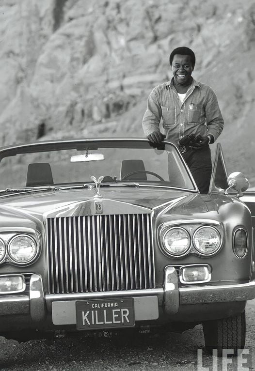 Comedian Flip Wilson standing next to his 1972 Rolls Royce, Corniche Convertible